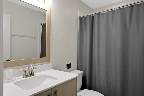 Un baño con lavamanos blanco, un espejo y cortina de ducha.