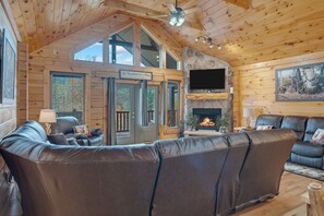 A log cabin interior with a leather sofa, a fireplace, and a television mounted on the wall. - Walden's Ridge Cabin 4 Bedroom Cabin (Sevierville)