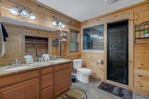 A wooden cabin-style bathroom with a large mirror, two sinks, a toilet, and a shower. - Walden's Ridge Cabin 4 Bedroom Cabin (Sevierville)