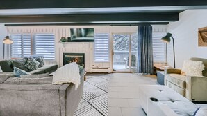 A modern living room with a fireplace, a sofa, a chair, and a large window with blinds. - The Lift B107 2 Bedroom Condo (Breckenridge)
