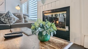 A living room with a green plant in a vase, a fireplace, a couch, and a coffee table with remotes. - The Lift B107 2 Bedroom Condo (Breckenridge)