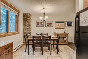A kitchen with a dining table, chairs, a chandelier, and a refrigerator. - Ski Hill 23 2 Bedroom Condo (Breckenridge)