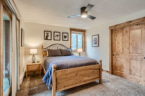 A bedroom with a wooden bed, a ceiling fan, a window with curtains, and a wooden door. - Ski Hill 23 2 Bedroom Condo (Breckenridge)