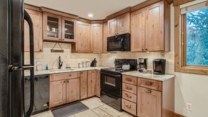 A modern kitchen with wooden cabinets, a black refrigerator, a microwave, a stove, and a coffee maker.