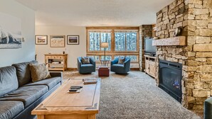 A cozy living room with a stone fireplace, a sofa, two armchairs, a coffee table, and a TV.