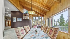 A wooden dining room with a long table, patterned cushions, and a hanging light fixture. - Mountain View Ski Lodge 5 Bedroom Townhouse (Breckenridge)