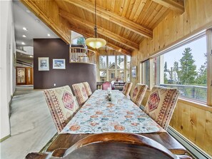 A wooden dining room with a long table, patterned cushions, and a hanging light fixture. - Mountain View Ski Lodge 5 Bedroom Townhouse (Breckenridge)