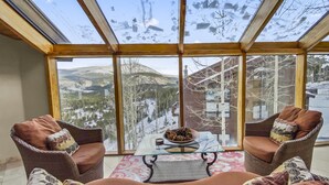 A cozy room with a large glass window overlooking a snowy mountain landscape. There are two wicker chairs and a small table with a bowl of pinecones. - Mountain View Ski Lodge 5 Bedroom Townhouse (Breckenridge)