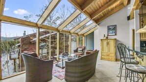 A spacious room with a high ceiling and large windows, featuring wicker furniture and a dining table. - Mountain View Ski Lodge 5 Bedroom Townhouse (Breckenridge)