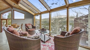 A spacious room with large windows offering a view of a mountainous landscape. There are wicker chairs and a table with a bowl of pinecones. - Mountain View Ski Lodge 5 Bedroom Townhouse (Breckenridge)