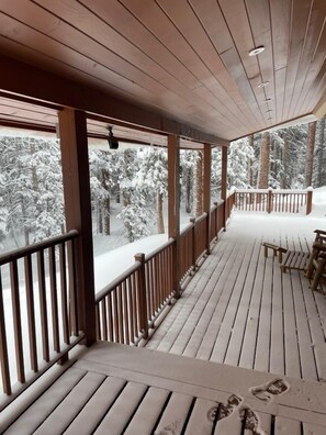 A wooden deck with railings, a bench, and a view of snow-covered trees.