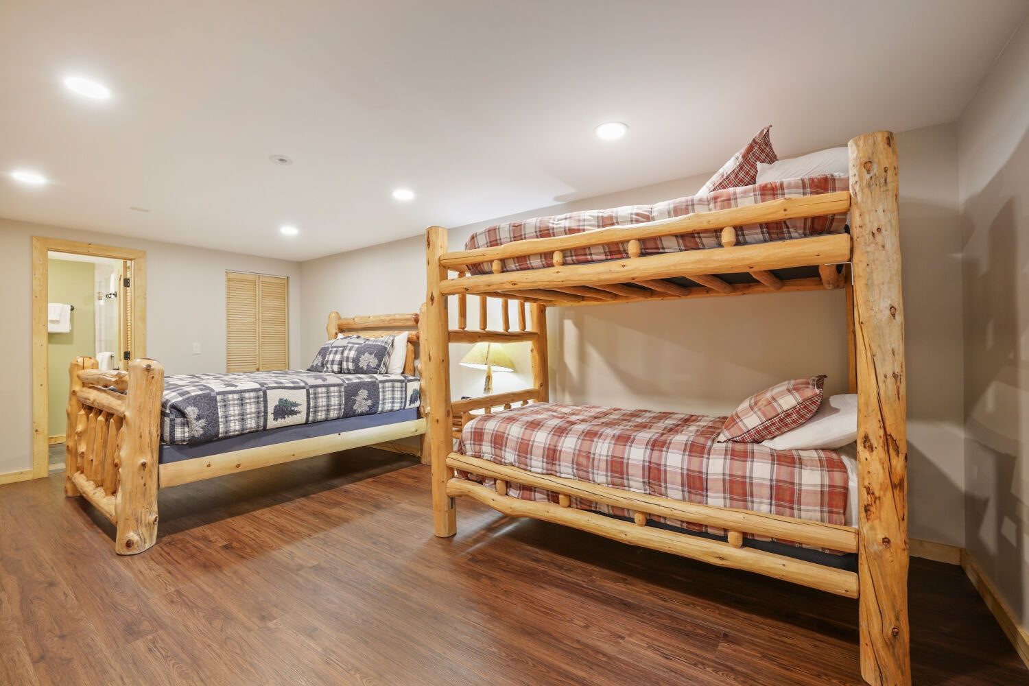 A room with two bunk beds, wooden flooring, and a door leading to a bathroom.