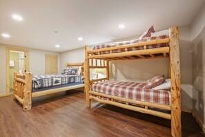 A room with two bunk beds, wooden flooring, and a door leading to a bathroom.