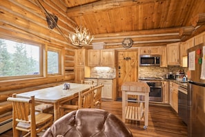 L’intérieur d’une cabane en rondins comprend un coin repas, une cuisine et une grande fenêtre donnant sur la forêt.