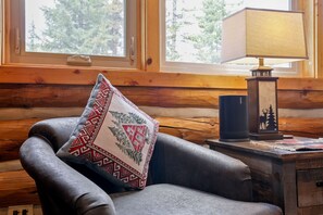 Interno di una baita in legno con una poltrona in pelle, un cuscino decorativo a motivi, una lampada e un tavolino con un oggetto ornamentale.