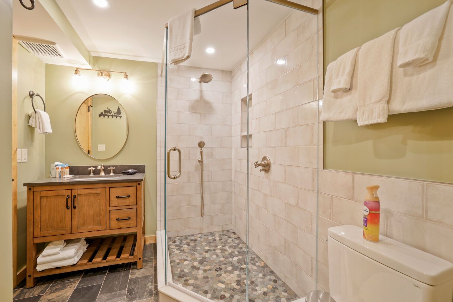 A bathroom with a glass-enclosed shower, a wooden vanity with a mirror, and a toilet.