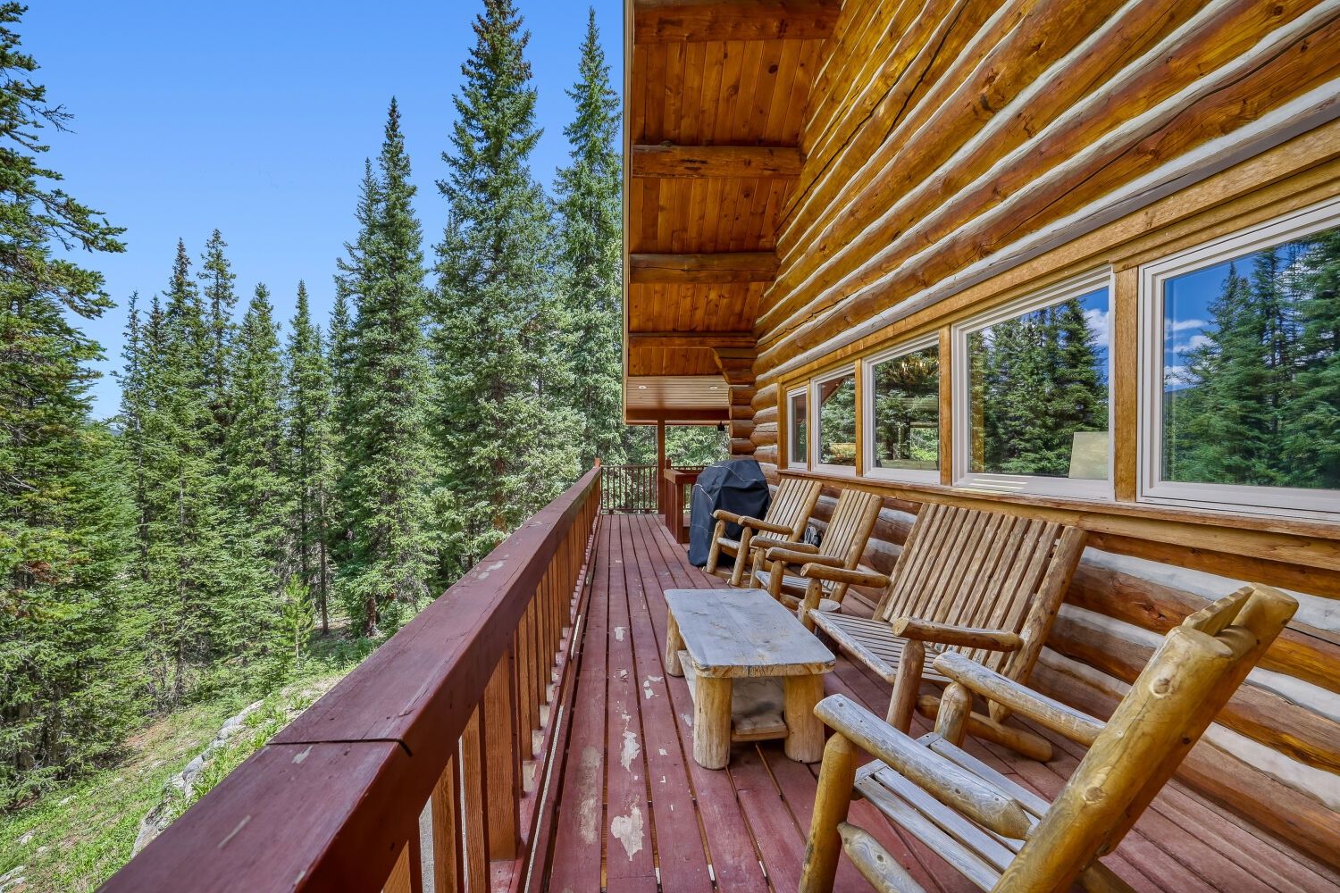 Une terrasse en bois avec une table et des chaises, donnant sur une zone boisée.