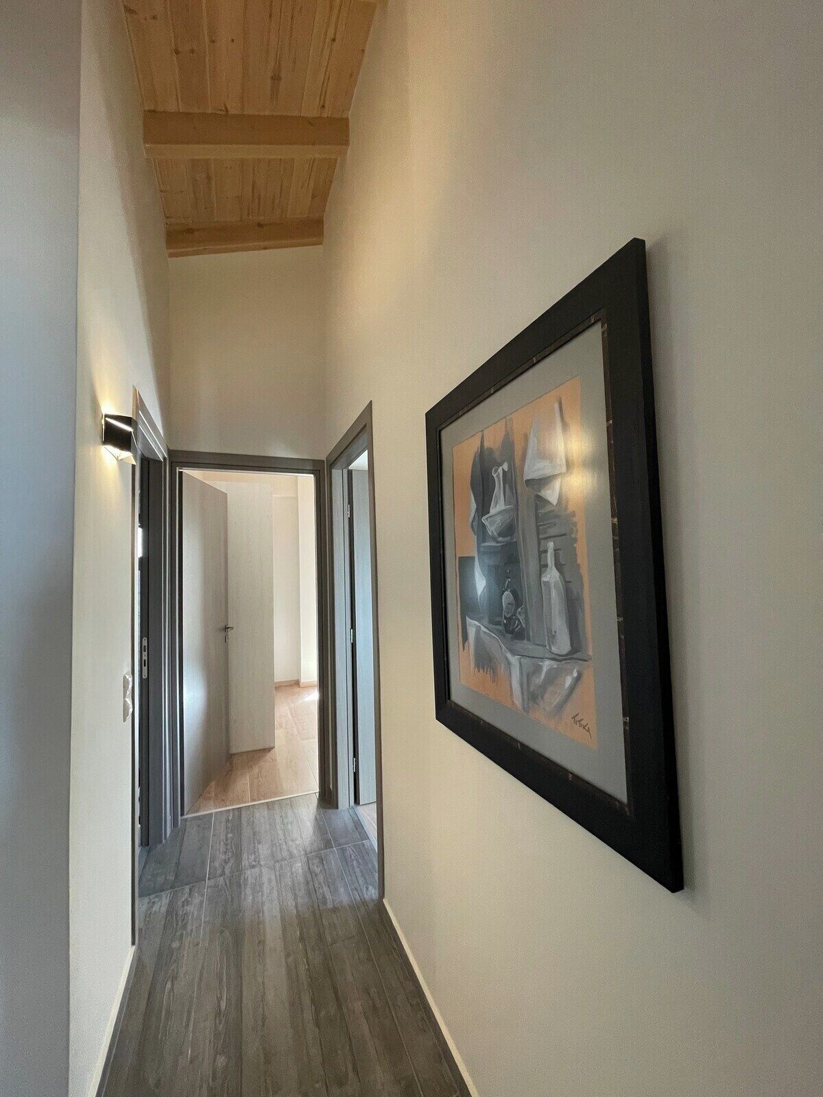Een hal met een houten plafond, een lijst met een abstract schilderij aan de muur en een deur die naar een andere kamer leidt.