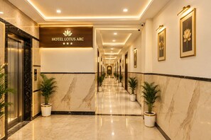 A hotel corridor with a marble floor, potted plants, and framed artwork on the walls. - Hotel Lotus Arc (New Delhi)