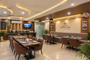 A hotel restaurant with a buffet, seating areas, and a television screen. - Hotel Lotus Arc (New Delhi)
