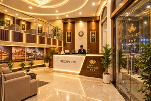 A hotel reception area with a marble floor, a reception desk, and a receptionist. - Hotel Lotus Arc (New Delhi)