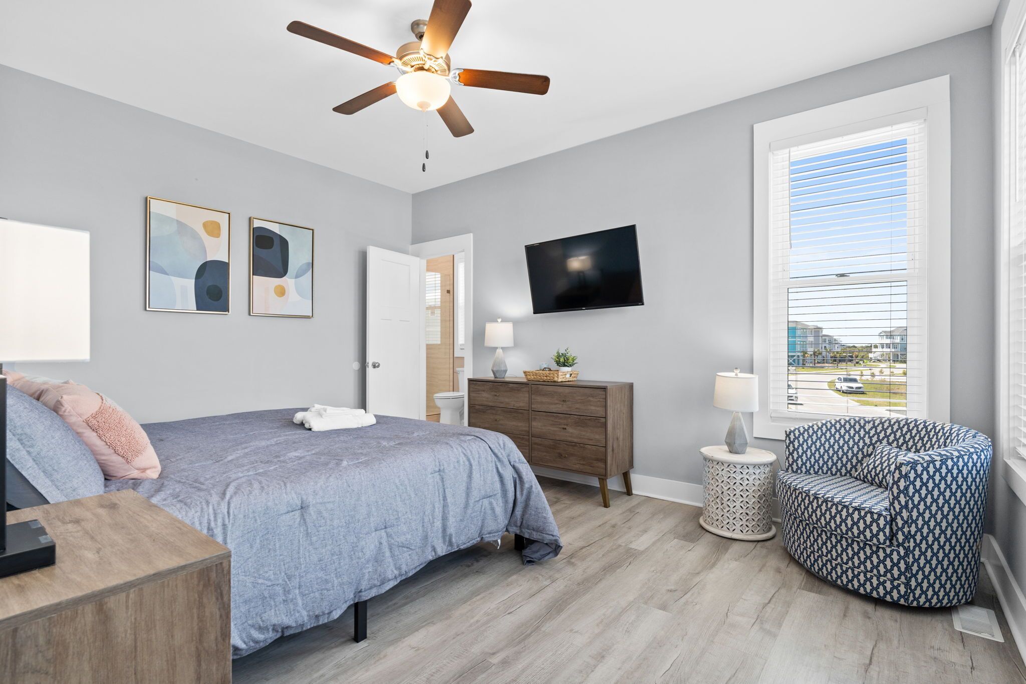 A bedroom with a bed, a ceiling fan, a TV, a window with blinds, and a chair.