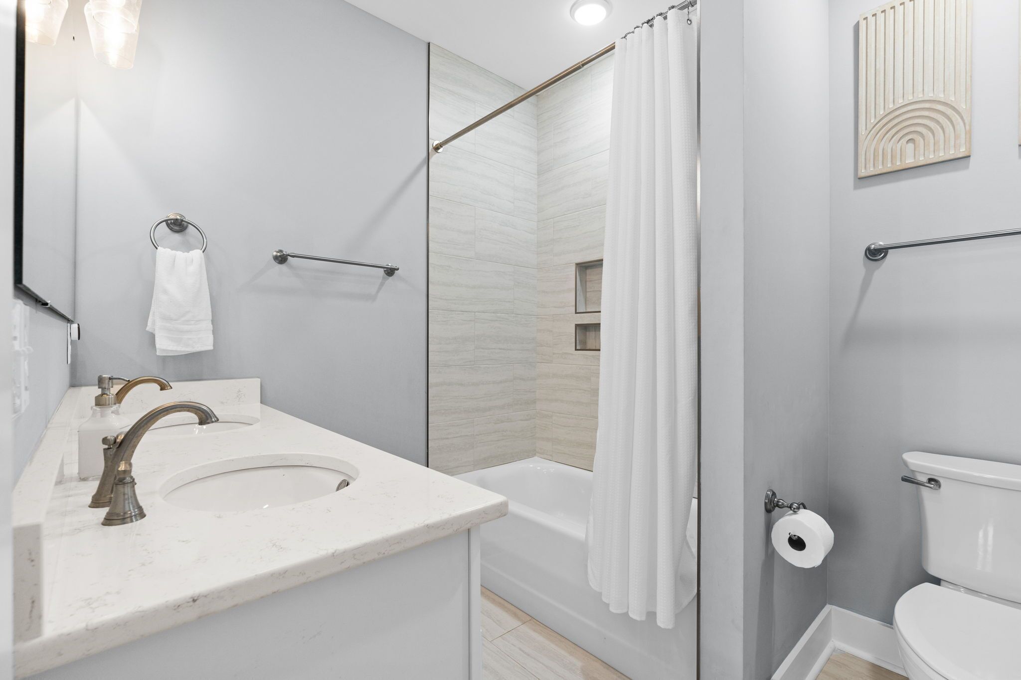 Un bany modern amb un lavabo, mirall, vàter i zona de dutxa.