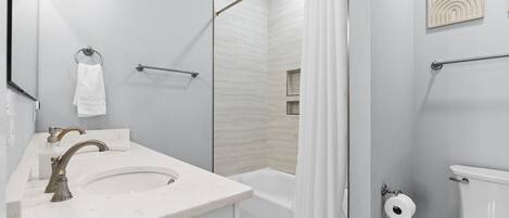 Un bany modern amb un lavabo, mirall, vàter i zona de dutxa.