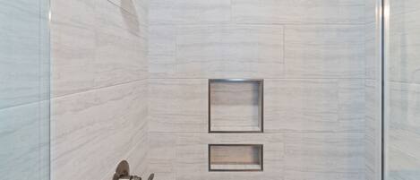 A modern shower with a handheld showerhead, a glass door, and a tiled wall with two rectangular cutouts.