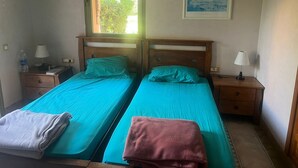 Een kamer met twee bedden, een raam, een schilderij en een waterfles op een nachtkastje.