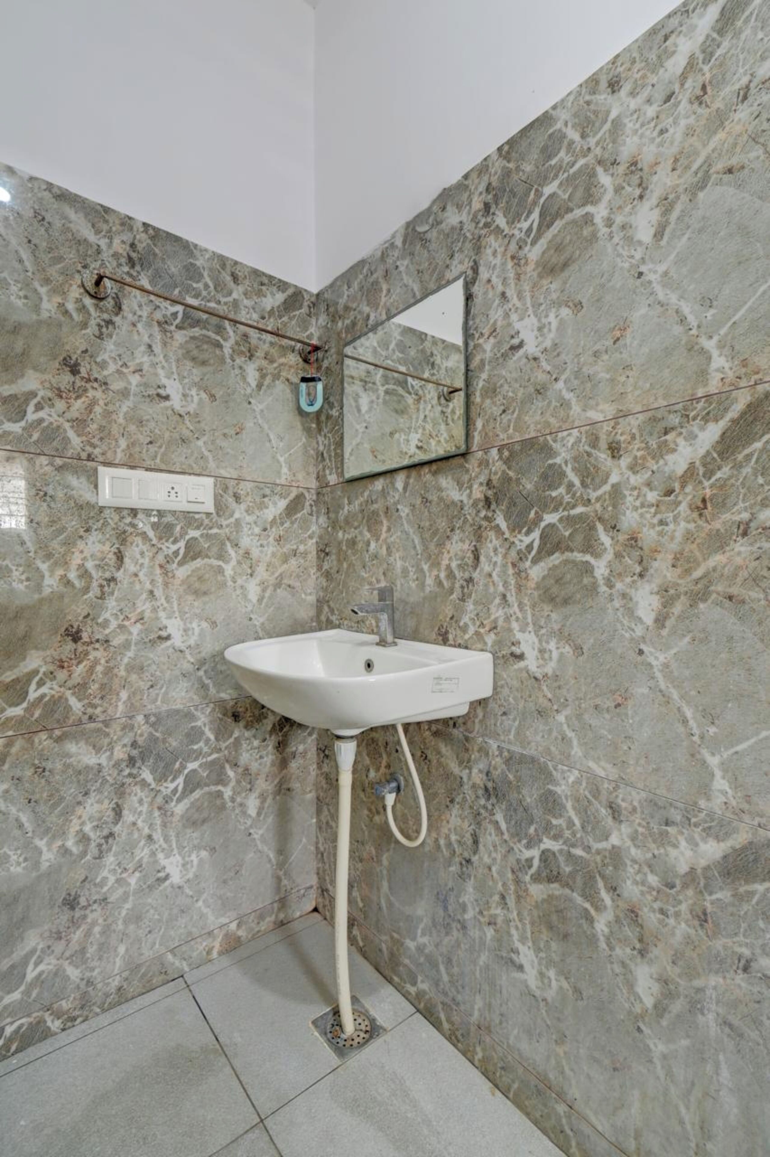 A bathroom with a marble wall, a white sink, and a mirror.
