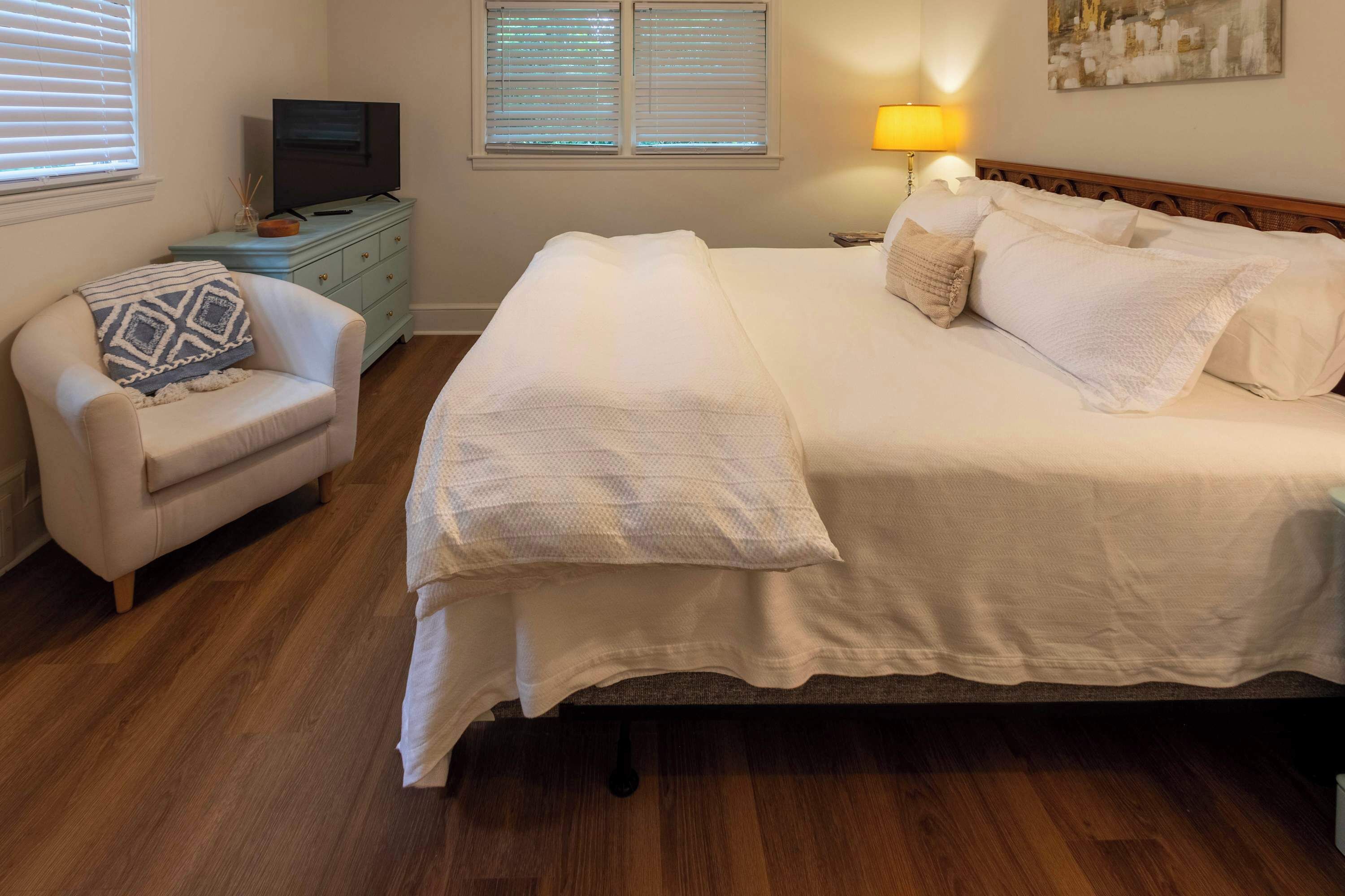 Ein ordentlich eingerichtetes Schlafzimmer mit Bett, Sessel, Kommode, Fernseher und Lampe.