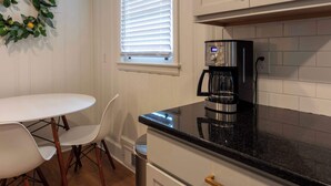 A kitchen with a white table and chairs, a coffee maker, and a window with blinds.