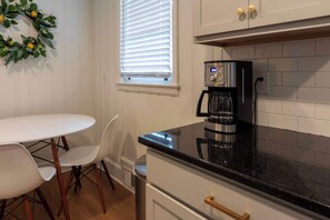 A kitchen with a white table and chairs, a coffee maker, and a window with blinds.