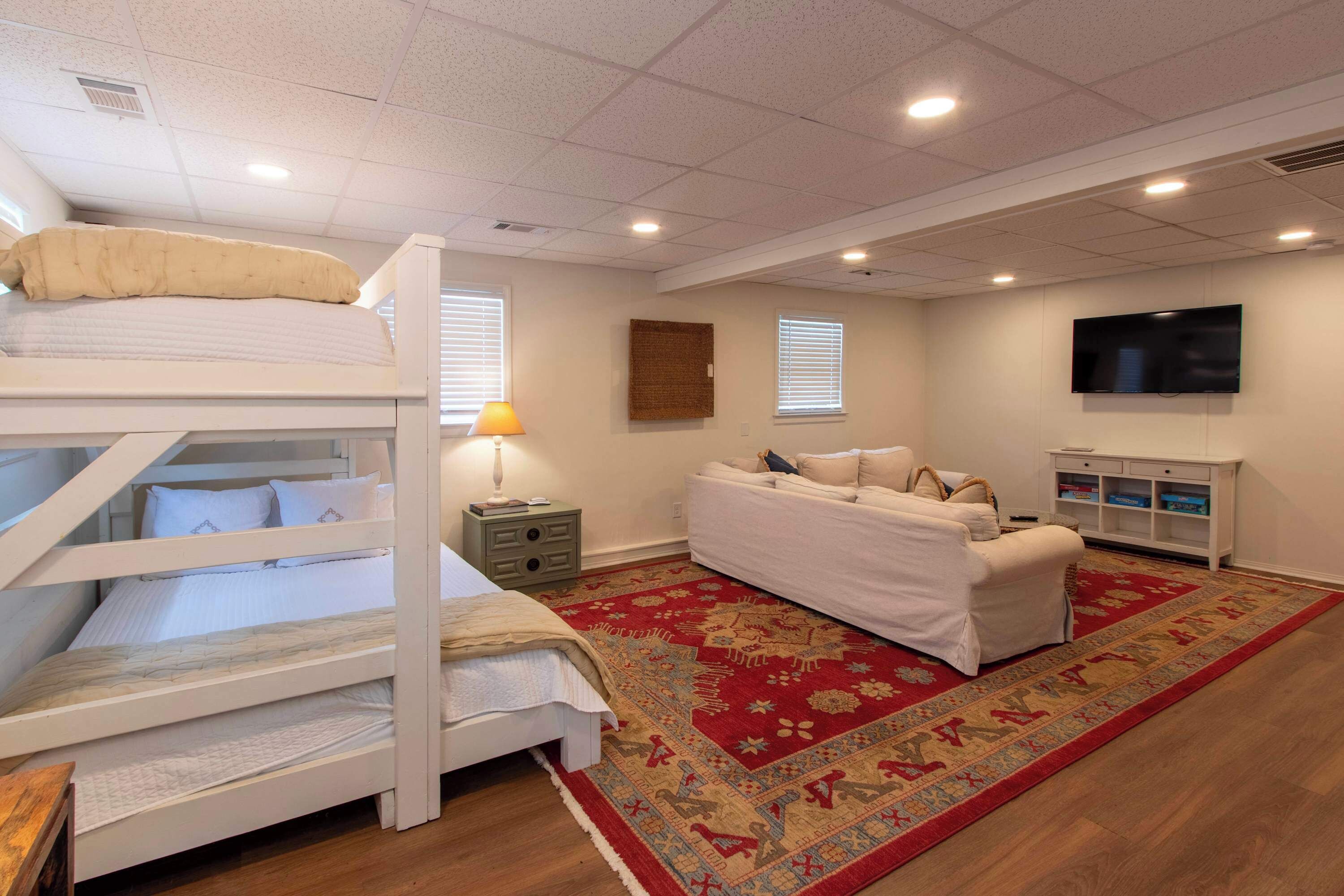 A room with bunk beds, a sofa, a TV, and a patterned rug.