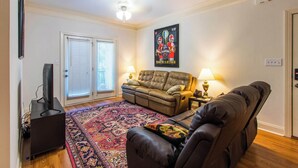 Un salon avec un canapé en cuir marron, un tapis à motifs, un téléviseur posé sur un meuble et une affiche accrochée au mur.