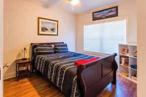 Un dormitorio con cama, mesita de noche, estantería y ventana con persianas.