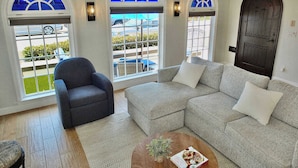 A living room with a grey sofa, a dark armchair, and a coffee table with a book and a plant.