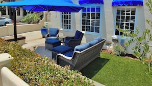 A patio with wicker furniture and blue cushions, a large potted plant, and a blue umbrella.