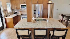 A modern kitchen with wooden cabinets, stainless steel appliances, a central island with seating, and a dining area.