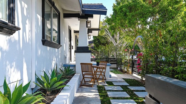 Una casa moderna con fachada blanca, un camino de piedra y un banco de madera.