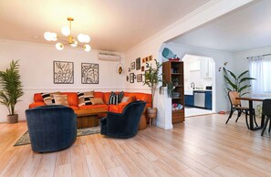 Un salon moderne avec un canapé, deux fauteuils, une table à manger et une cuisine en arrière-plan.