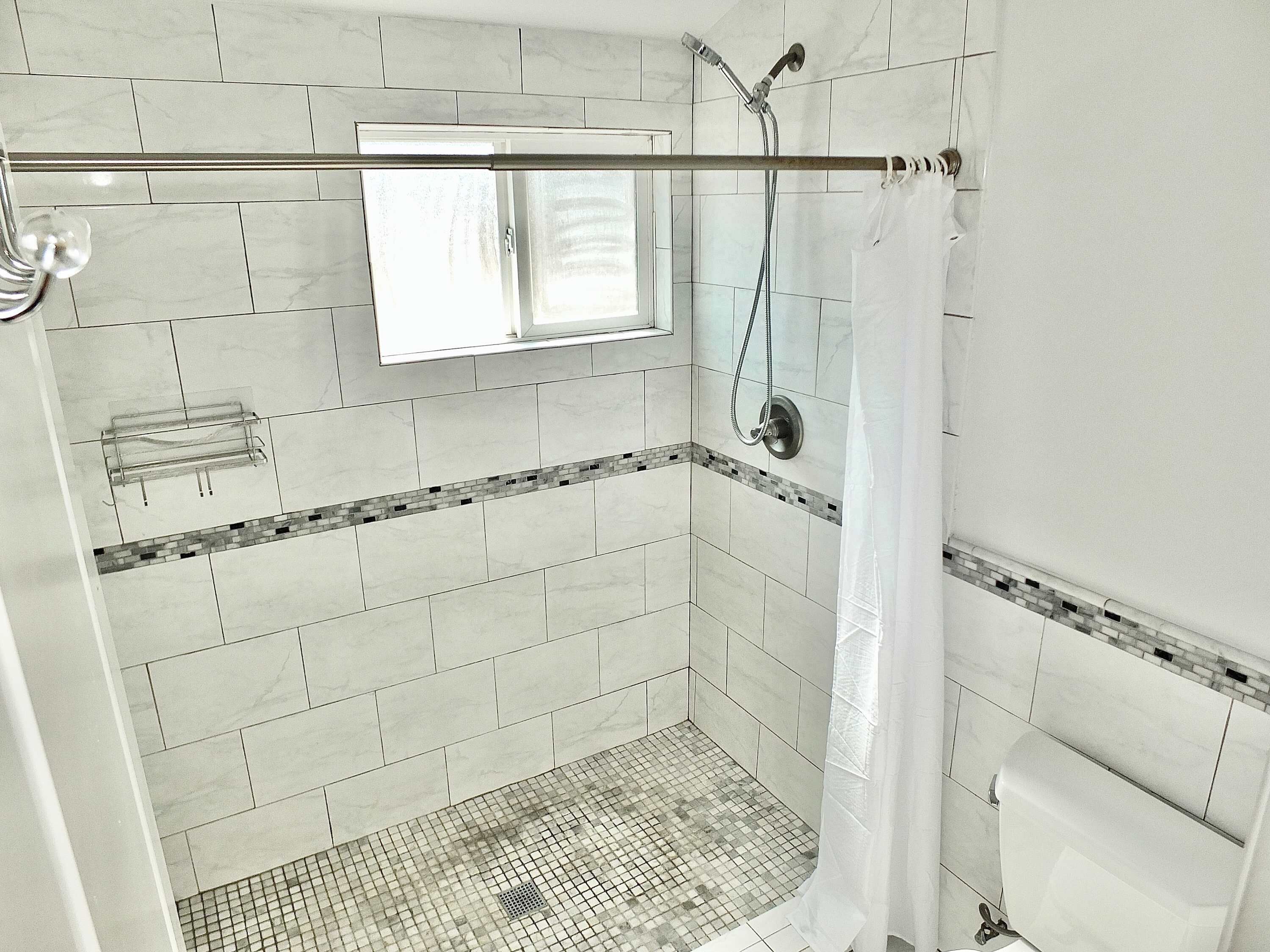 A shower area with a glass door, a showerhead, and a tiled floor.