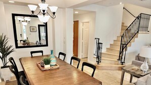 A spacious dining area with a wooden table, black chairs, and a chandelier. A staircase with a black railing leads to another level. - New Remodel, Rooftop Deck, Sleeps 8+ (Long Beach)