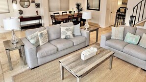 A spacious living room with a grey sofa, a wooden coffee table, and a dining area with a wooden table and chairs. - New Remodel, Rooftop Deck, Sleeps 8+ (Long Beach)
