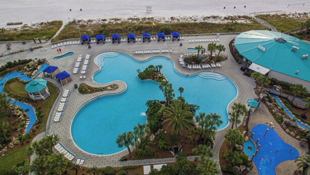 An aerial view of a resort with a large central pool, multiple smaller pools, and a beach area.