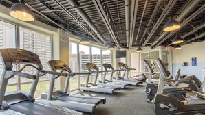 Un gimnasio con cintas de correr, bicicletas estáticas y un amplio ventanal con vistas a edificios.