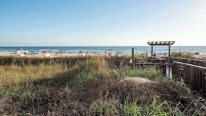 A beach with a wooden boardwalk leading to a covered area, sandy beach, and clear blue sky.