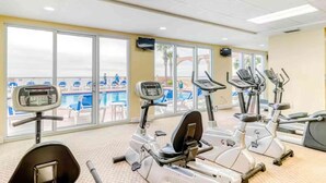 Un gimnasio con bicicletas estáticas y cintas de correr, amplias ventanas con vistas a la piscina.