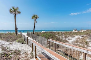 A beach with a wooden boardwalk, palm trees, and a beach umbrella in the background.